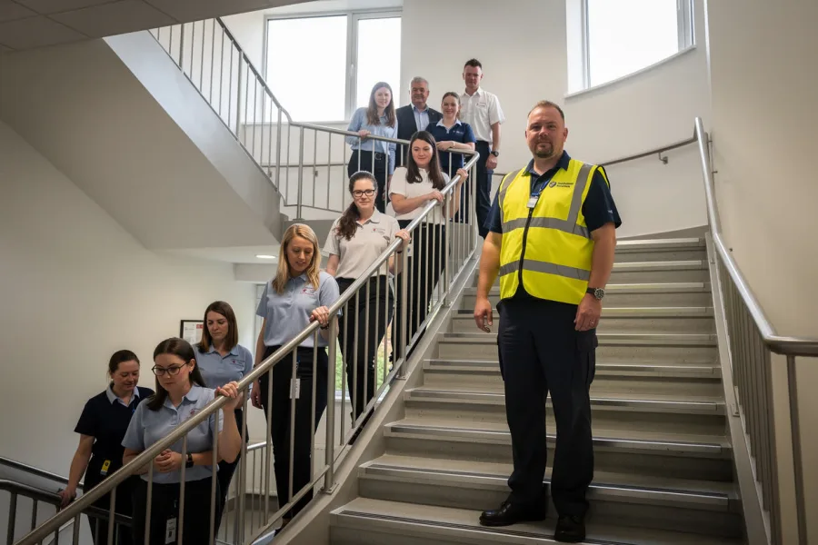 Des travailleurs descendent un escalier pendant une évacuation, sous le regard d'un collègue en gilet de sécurité